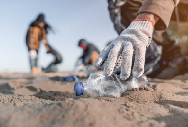 Mano guantata raccoglie una bottiglia di plastica usata gettata sulla spiaggia